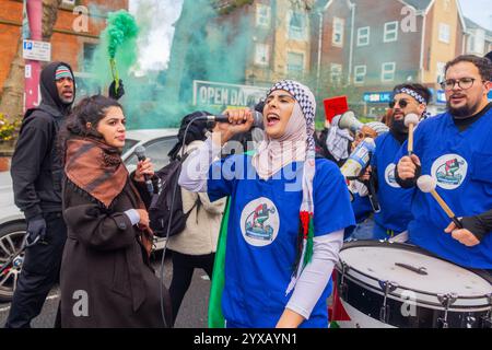 Birmingham, Royaume-Uni. 14 DEC, 2024. Taby Khan, scientifique et activiste dirige le chant alors qu'une foule pro Palestine marchait du parc Handsworth au centre de Birmingham, le groupe, y compris ceux qui portaient des gommages dans le cadre de Healthworkers 4 Palestine chantait et allumait des fusées éclairantes. Des groupes de Liverpool et de Londres se sont joints. Crédit Milo Chandler/Alamy Live News Banque D'Images