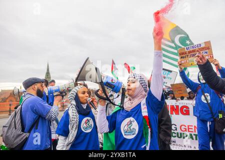 Birmingham, Royaume-Uni. 14 DEC, 2024. Taby Khan, scientifique et activiste dirige le chant alors qu'une foule pro Palestine marchait du parc Handsworth au centre de Birmingham, le groupe, y compris ceux qui portaient des gommages dans le cadre de Healthworkers 4 Palestine chantait et allumait des fusées éclairantes. Des groupes de Liverpool et de Londres se sont joints. Crédit Milo Chandler/Alamy Live News Banque D'Images