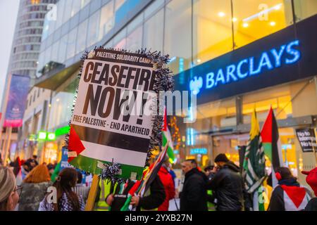 Birmingham, Royaume-Uni. 14 DEC, 2024. Des panneaux placés près du logo Barclays alors que des discours se tenaient à l'extérieur après la marche Pro Palestine du parc Handsworth au centre de Birmingham, le groupe, y compris ceux portant des gommages dans le cadre de Healthworkers 4 Palestine, a chanté et allumé des fusées éclairantes. Des groupes de Liverpool et de Londres se sont joints. Crédit Milo Chandler/Alamy Live News Banque D'Images