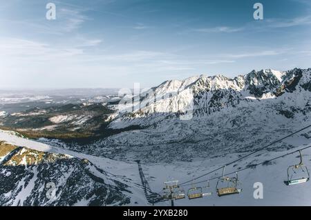 Télésiège transportant les skieurs et les snowboarders sur une pente de montagne enneigée à zakopane, en pologne, avec une vue imprenable sur les sommets et les vallées environnants Banque D'Images