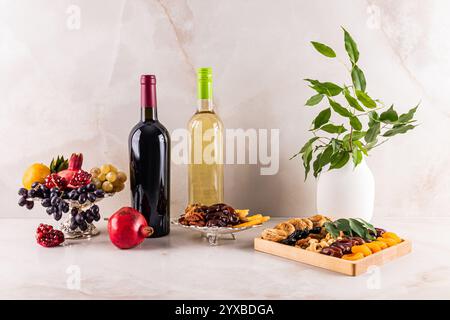 Nature morte festive sur un comptoir en marbre à tu bi shvat avec deux bouteilles de vin, des fruits frais dans un vase en argent, des fruits secs. branches de l'arbre Banque D'Images