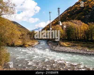 Fond de ruisseau d'été avec deux tours de télécommunication près des montagnes sur fond de ciel bleu. L'eau se précipite à travers le ruisseau rocheux sur le h. Banque D'Images