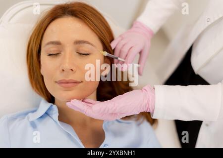 Le patient se détend sur un lit de traitement confortable tandis qu'un praticien qualifié applique un produit de remplissage dermique pour améliorer les traits du visage dans une clinique tranquille envi Banque D'Images