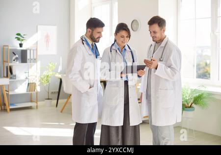 Médecins regardant l'écran de tablette discutant du traitement debout à l'hôpital ou à la clinique. Banque D'Images
