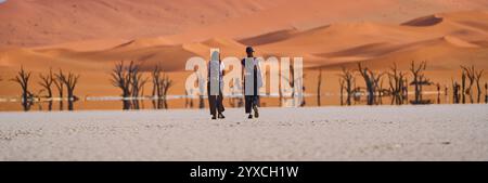 Une image panoramique haute résolution de deux femmes marchant à travers le plan blanc vers les arbres pétrifiés à Deadvlei, Namibie, Afrique Banque D'Images
