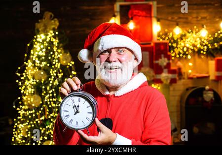 Joyeux Père Noël tenant l'horloge montrant cinq minutes à minuit. Compte à rebours du nouvel an. Homme barbu en vêtements de Père Noël avec horloge du nouvel an. Père Noël avec Banque D'Images