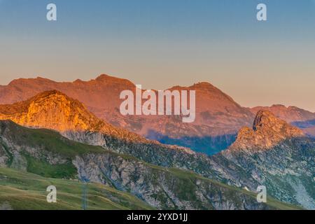 Coucher de soleil dans les montagnes. Lumière rouge sur le ciel avec quelques nuages au-dessus des magnifiques sommets montagneux et des sommets enneigés des Alpes. De beaux cieux brûlants Banque D'Images