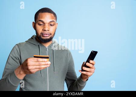 Heureux homme afro-américain excité faisant un achat en ligne avec une carte de crédit, en entrant les identifiants bancaires pour payer quelque chose sur la promotion. Jeune homme confiant faisant des achats sur internet. Banque D'Images