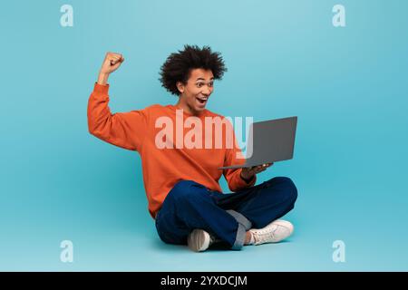 Jeune homme afro-américain célèbre le succès tout en utilisant son ordinateur portable Banque D'Images