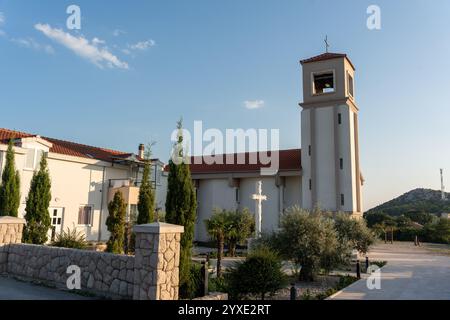 Église moderne avec clocher, monument à croix blanche et jardin luxuriant entouré d'oliviers et de grands cyprès. Concept de paisible Ar Banque D'Images