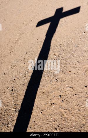 Une représentation poétique de l’ombre d’une croix sur un sol désertique, illustrant le message universel d’espérance, de foi et de sacrifice de Jésus pour l’humanité Banque D'Images