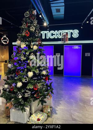 Kiev, Ukraine - 15 décembre 2024 : un sapin de Noël orné d'ornements et de cadeaux dans une zone de billets élégante illuminée de néons vibrants et festifs Banque D'Images