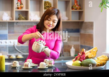 Une femme vietnamienne d'âge moyen dans une robe rouge prépare le thé traditionnel vietnamien au bar d'un café Banque D'Images