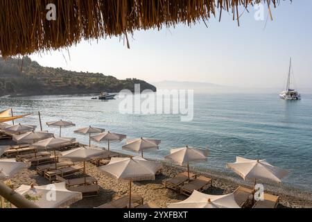 Chaises longues et parasols en rotin sur la plage. Chaises longues et parasols en rotin sur le bord de mer sablonneux. Chaise parasol et salon sur la belle plage. Banque D'Images