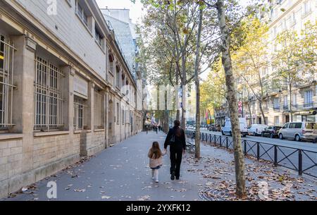 Une femme avec une petite fille marchant dans la rue à Paris avec de beaux bâtiments et des voitures garées. Paris, France - 30 octobre 2024 Banque D'Images