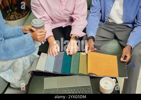 Plan recadré d'un groupe diversifié de trois designers d'intérieur choisissant le tissu sur des échantillons de différentes couleurs tout en travaillant en collaboration à table dans le salon de coworking Banque D'Images