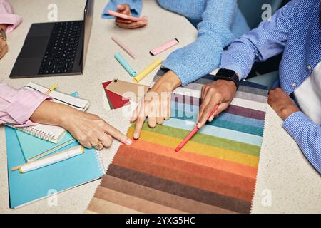 Plan recadré de l'équipe diversifiée de concepteurs choisissant le tissu parmi divers échantillons de couleur sur la table tout en travaillant en collaboration sur un nouveau projet sur le lieu de travail, copier SPAC Banque D'Images