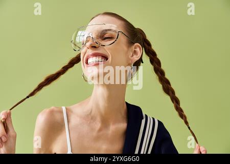 Une jeune femme avec des tresses exprime la joie en souriant largement sur un fond vert vibrant. Banque D'Images