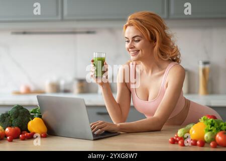 Jeune femme aime smoothie sain tout en travaillant sur ordinateur portable à la cuisine à la maison Banque D'Images