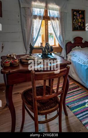 Sanok, Pologne - 4 mai 2024. Une machine à coudre vintage se trouve sur un bureau en bois dans une salle rustique avec des murs blancs et un plancher en bois au Museum of Folk Banque D'Images