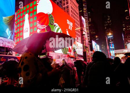 Les visiteurs de Times Square à New York le mercredi 11 décembre 2024 marchent sous la pluie sous les panneaux publicitaires numériques sur le thème de Noël faisant la publicité de Coca-Cola. (© Richard B. Levine) Banque D'Images