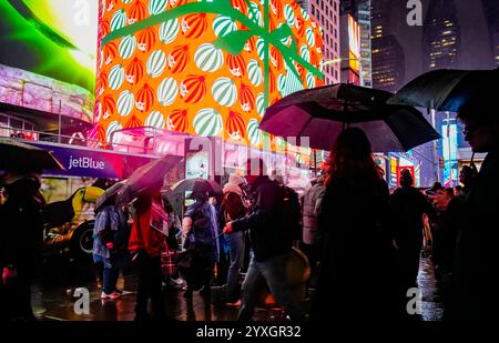 Les visiteurs de Times Square à New York le mercredi 11 décembre 2024 marchent sous la pluie sous les panneaux publicitaires numériques sur le thème de Noël faisant la publicité de Coca-Cola. (© Richard B. Levine) Banque D'Images