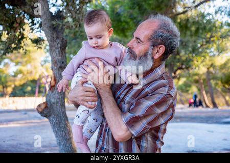 Un moment touchant capturé entre grand-père et petit-enfant partageant une douce étreinte dans la lumière dorée de la nature, mettant en valeur le lien magnifique entre eux Banque D'Images