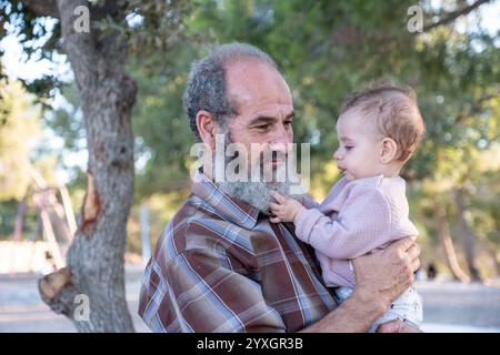 Un moment touchant capturé entre grand-père et petit-enfant partageant une douce étreinte dans la lumière dorée de la nature, mettant en valeur le lien magnifique entre eux Banque D'Images