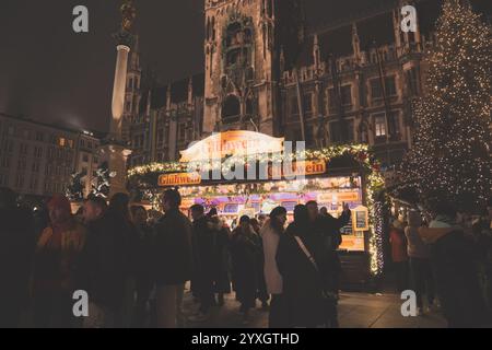 Munich, Allemagne - 1er décembre 2024 : stand vendant du vin chaud gluhwein sur un marché de Noël à Munich la nuit, des foules de gens devant le rath Banque D'Images