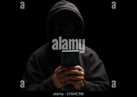 Hacker dans la capuche noire tenant un téléphone mobile, Scam concept de cybercriminalité Banque D'Images