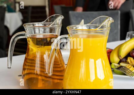 Jus de pomme et d'orange dans des pichets en verre pichets sur une table de restaurant avec plateau de fruits et arrière-plan flou du cadre de l'événement de restauration. Différents dri Banque D'Images