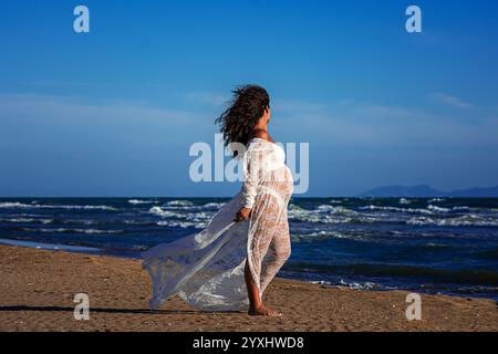 belle femme méditerranéenne aux cheveux bouclés enceinte pose sur la plage Banque D'Images