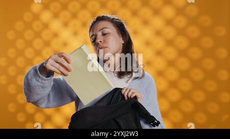 Portrait de femme fouillant à travers le sac à dos, prenant le livre, isolé sur fond de studio. Élève enlevant le manuel utilisé à des fins éducatives du sac à dos de l'école, appareil photo B. Banque D'Images