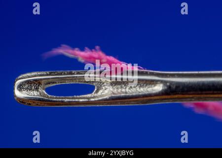 Oeil d'aiguille et fil à coudre rose sur fond bleu Banque D'Images