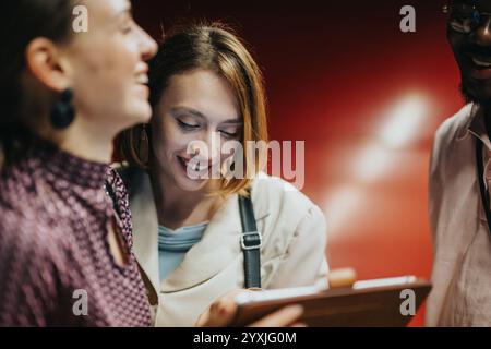 Groupe diversifié de collègues collaborant dans un environnement de bureau créatif tout en se tenant ensemble et en discutant avec enthousiasme des idées avec une tablette Banque D'Images