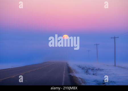 Le soleil couchant descendant dans un banc de brouillard sur la route 561 en Alberta, Canada. Banque D'Images