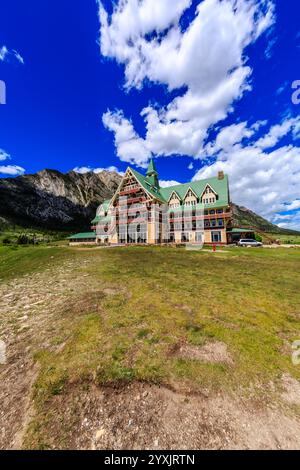 Une grande maison avec un toit vert se trouve sur une colline herbeuse. La maison est entourée d'un champ verdoyant et d'une montagne en arrière-plan. Le ciel est clair Banque D'Images