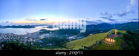 Une vue aérienne panoramique à couper le souffle de Coron, Philippines, capturée lors d'un coucher de soleil vibrant. L'image montre des collines verdoyantes, une grande croix an Banque D'Images