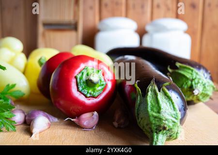 Les légumes colorés, y compris les poivrons, les aubergines et l'ail, sont disposés sur une planche à découper en bois. L'atmosphère chaleureuse de la cuisine rehausse le Banque D'Images