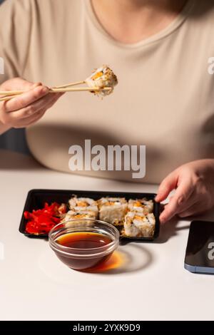 Femme mangeant des rouleaux de sushi avec des baguettes au travail. Nourriture asiatique saine pendant la pause déjeuner au travail. Sushi en paquet à emporter. Cuisine asiatique savoureuse Banque D'Images
