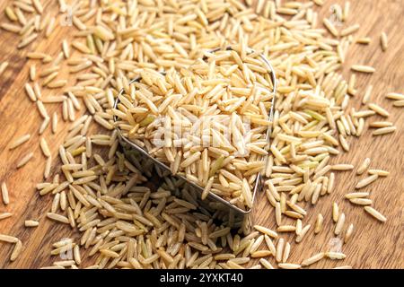 Grains de riz basmati crus non polis dispersés sur une surface en bois. Récipient métallique en forme de coeur rempli d'amandes rustiques non transformées. Gros plan. Haut v Banque D'Images