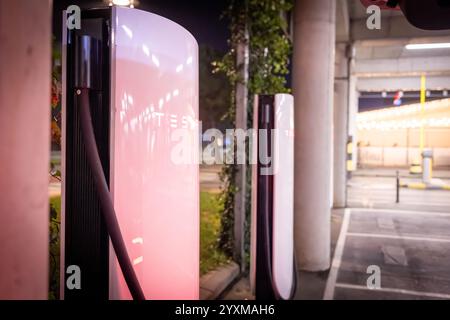 Une rangée de Superchargeurs Tesla éclairés la nuit dans un environnement urbain, mettant en valeur une technologie de recharge de véhicule électrique de pointe. Banque D'Images