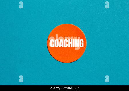 Message de coaching écrit sur un autocollant rond orange sur fond bleu. Symbole de coaching conceptuel. Copier l'espace. Banque D'Images