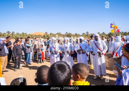 Merzouga, Maroc, 12, 6, 2023. Un mariage berbère traditionnel a lieu à la périphérie du village. Au centre un groupe de musiciens gnawa pla Banque D'Images