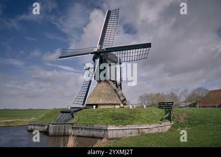 Moulin à vent historique Spinnenkop près de Nijhuizum en Frise, pays-Bas, entouré de champs verts, d'un canal et de nuages spectaculaires par une journée brillante. Banque D'Images