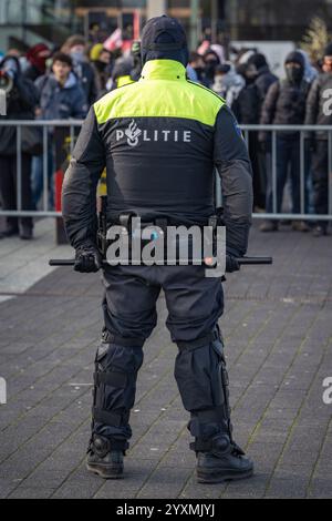 Rotterdam, pays-Bas, 21.11.2024, officier de police néerlandais face aux manifestants et tenant un bâton derrière son dos lors d'un rassemblement de protestation, vue arrière Banque D'Images