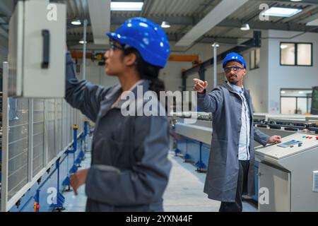 Deux ingénieurs, une indienne et un afro-américain, supervisant le travail des machines automatiques dans une usine industrielle. Banque D'Images