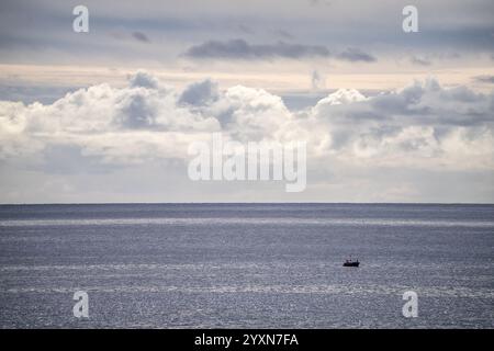 Une scène océanique tranquille avec un petit bateau et une vaste étendue de nuages, créant un paysage atmosphérique et paisible. Parfait pour les thèmes de soli Banque D'Images