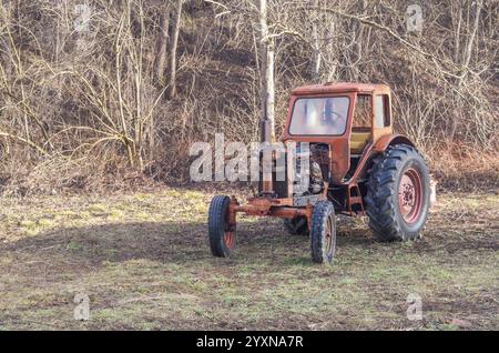 Un tracteur. Un vieux tracteur rouge rouillée dans une ferme dans les bois. Banque D'Images