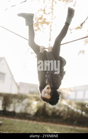 Fille suspendue à l'envers sur une corde de gymnastique à l'aire de jeux Banque D'Images